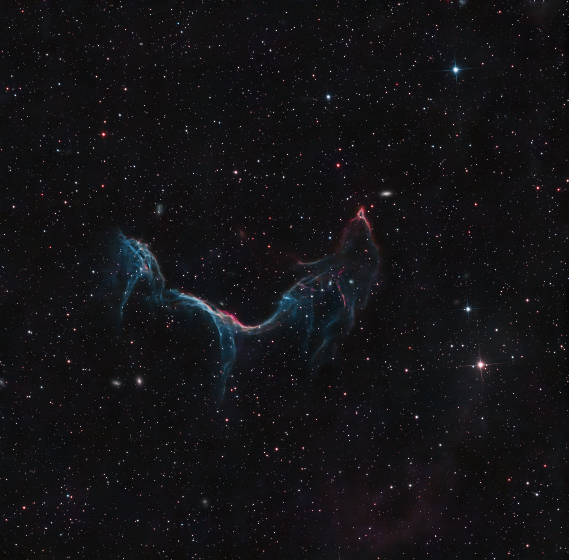 A thin blue and red supernova-remnant arc crossing a dark field of stars.