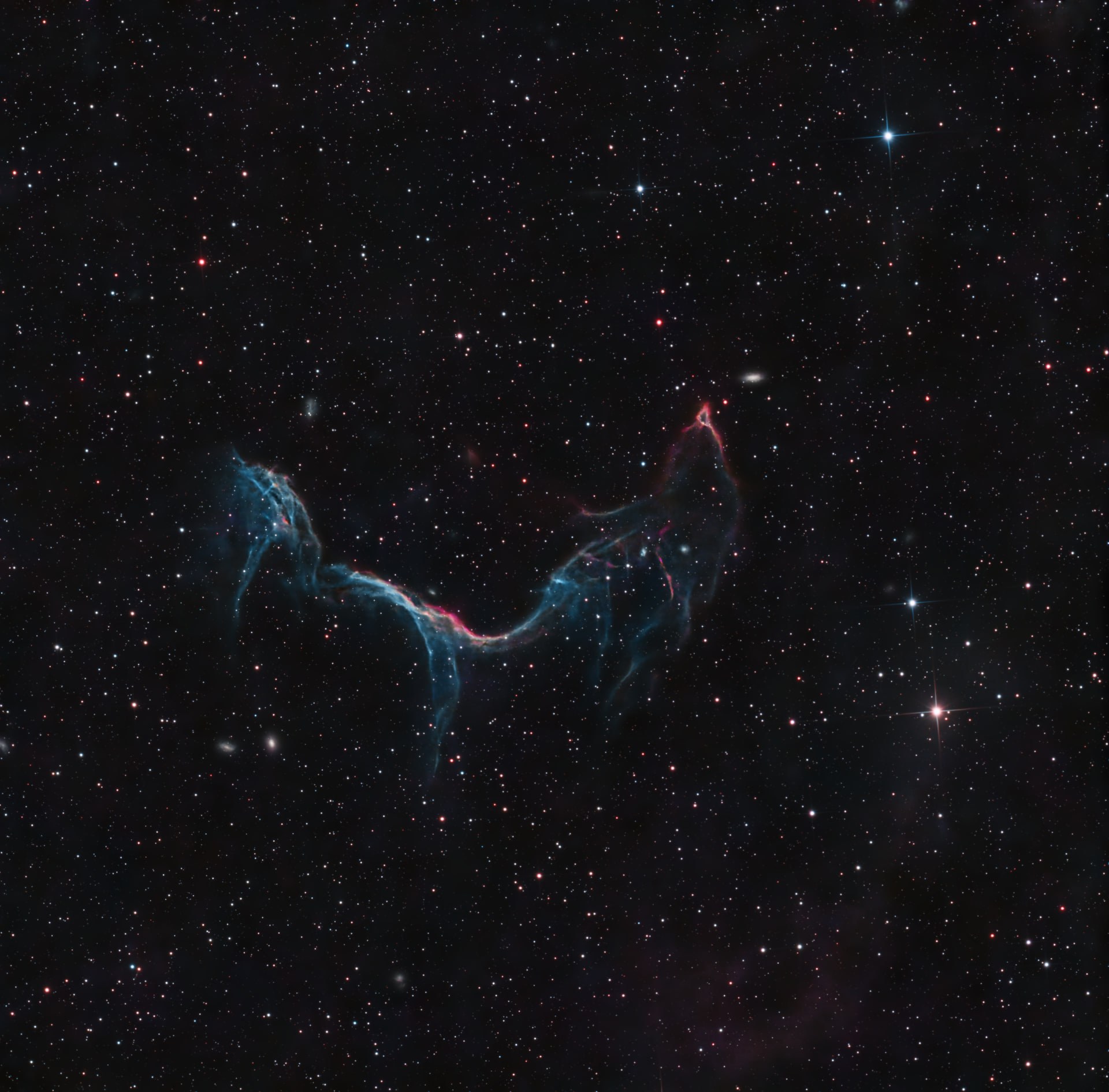 A thin blue and red supernova-remnant arc crossing a dark field of stars.