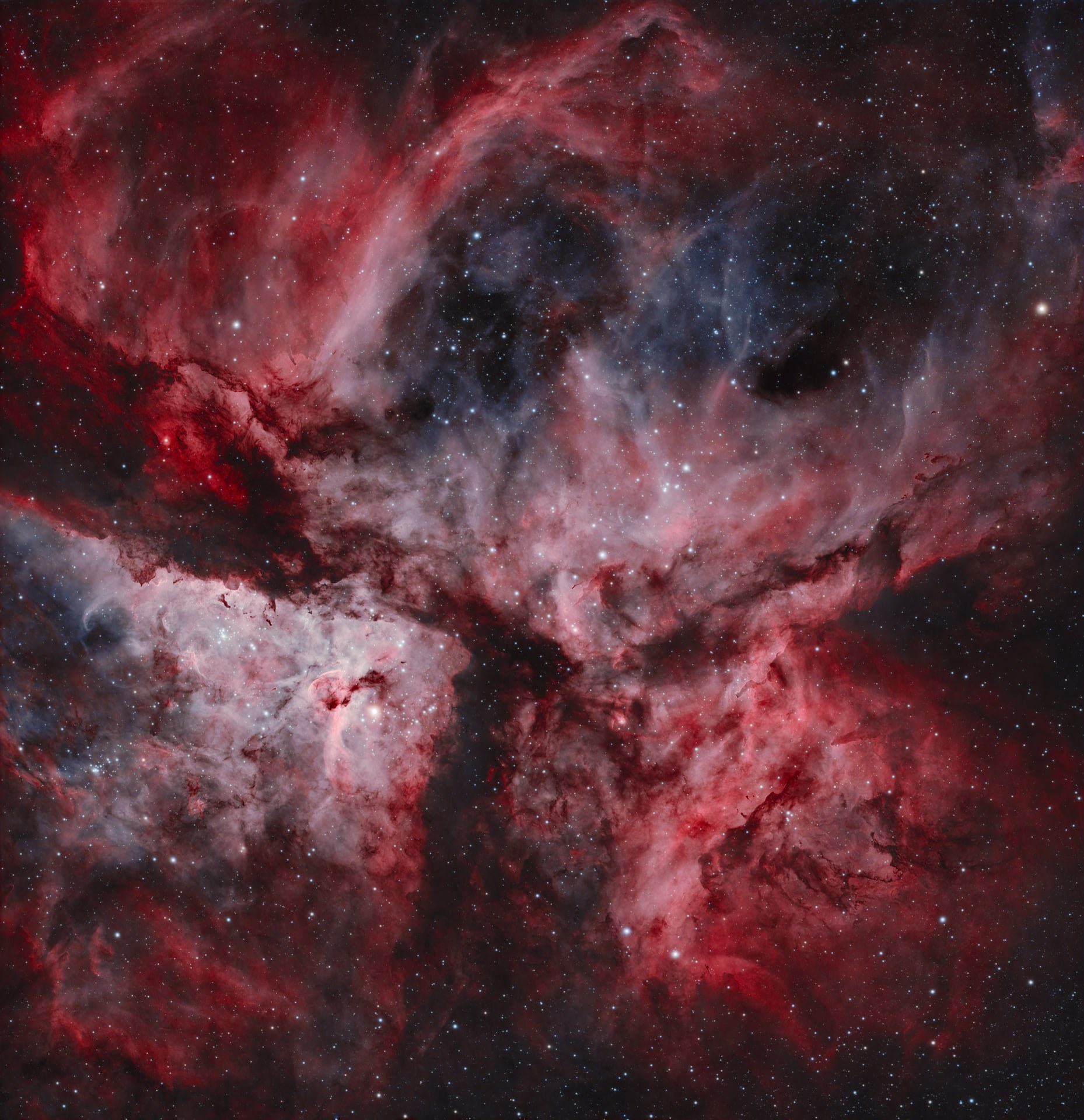 A dense red and charcoal view of the Carina Nebula filled with glowing gas and dark dust lanes.