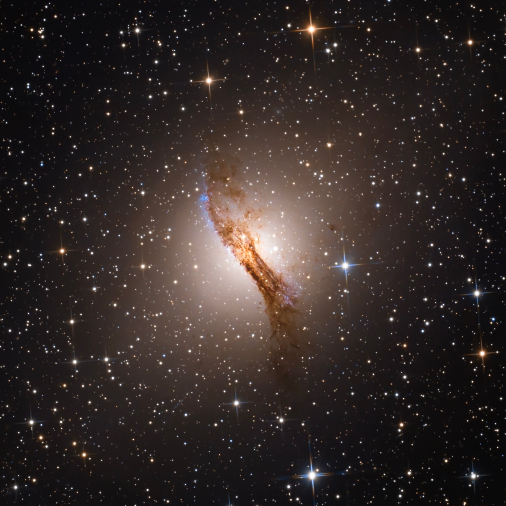 Centaurus A shining through a prominent dark dust lane in a field of foreground stars.