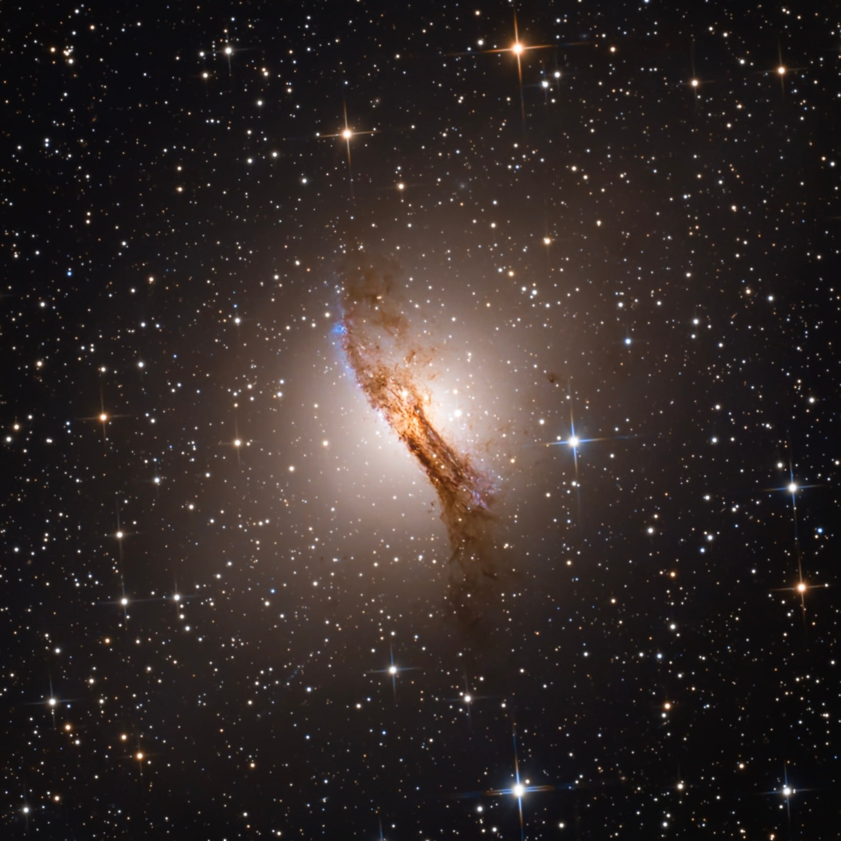 Centaurus A shining through a prominent dark dust lane in a field of foreground stars.