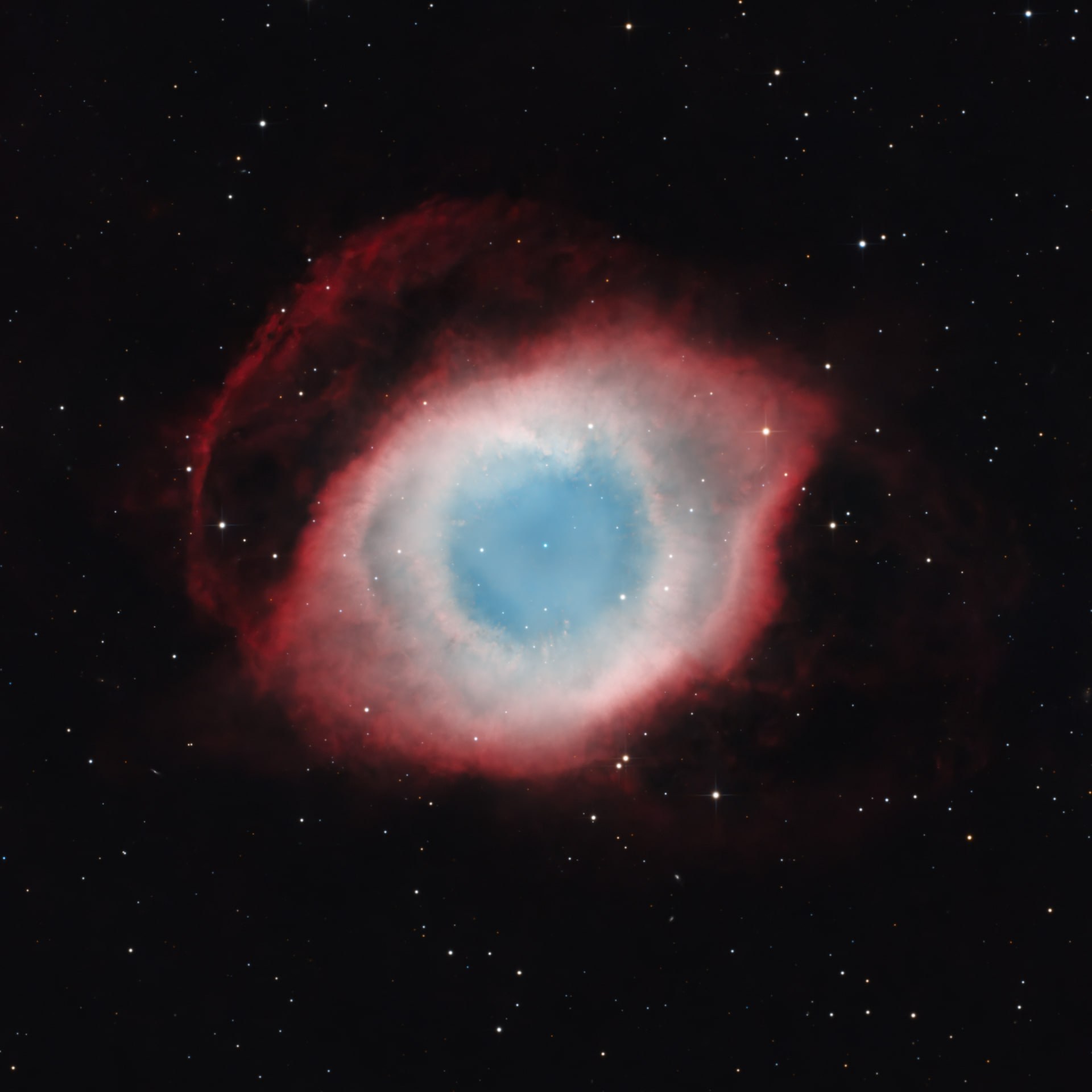 The Helix Nebula appearing as a blue-green eye encircled by a red outer shell.
