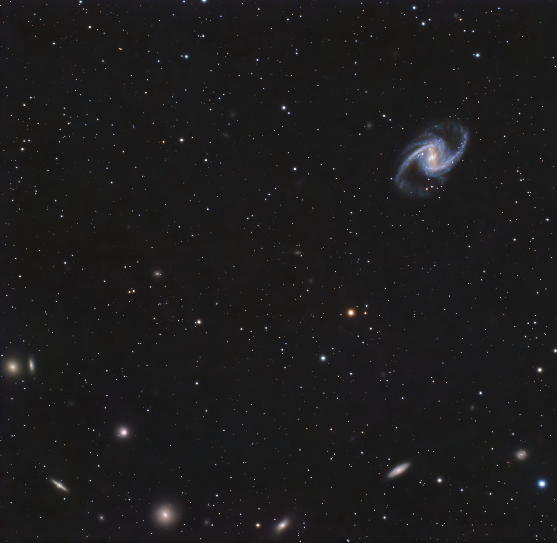The bright central bar and blue spiral arms of NGC 1365 in the upper right of a wide star field with smaller galaxies.