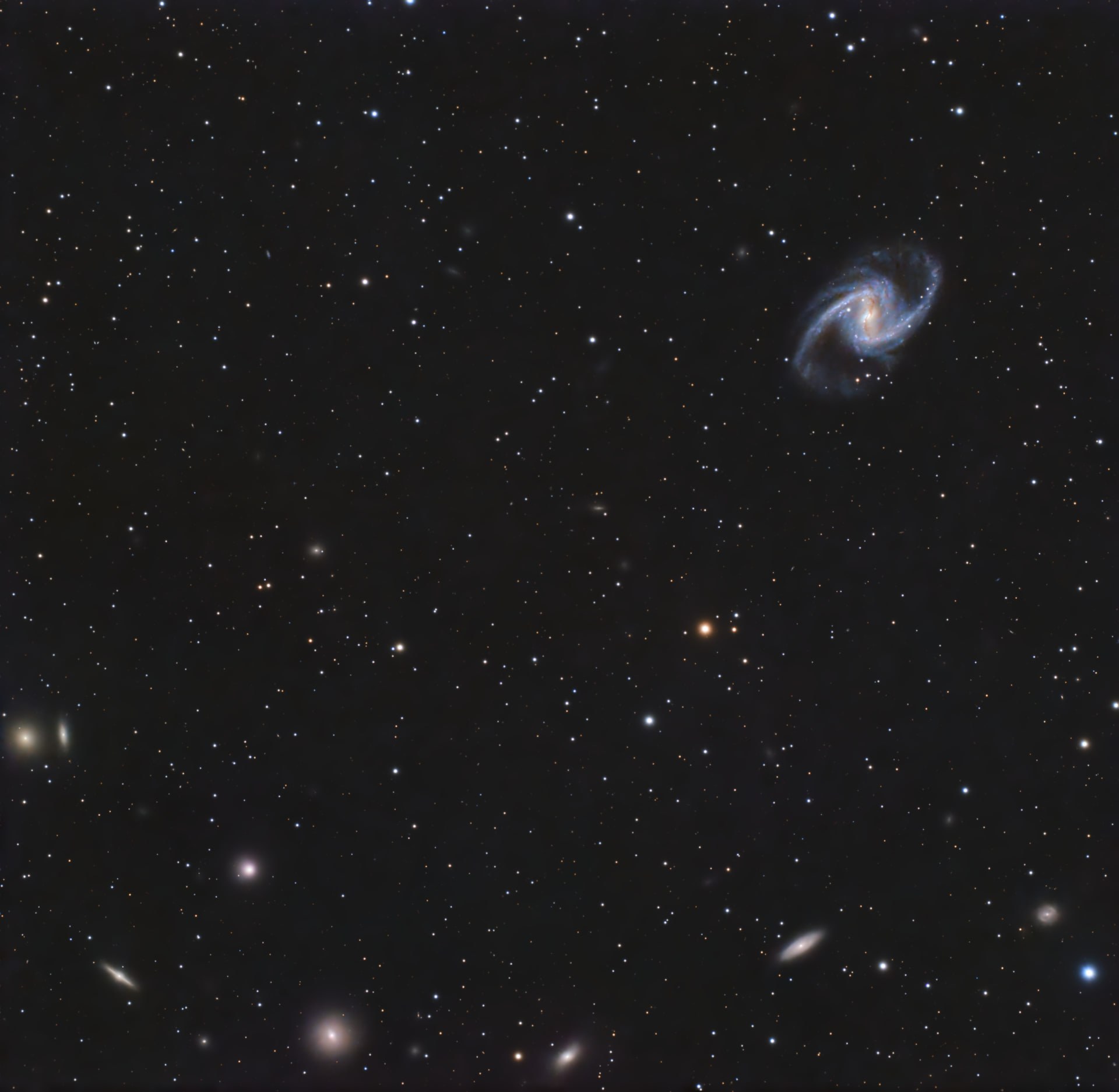 The bright central bar and blue spiral arms of NGC 1365 in the upper right of a wide star field with smaller galaxies.